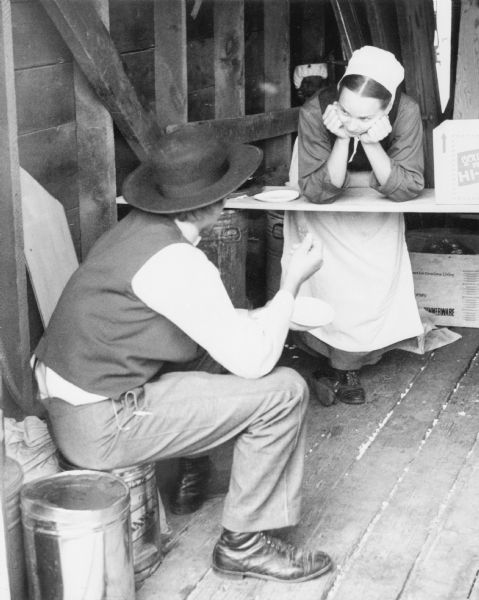 An Amish man and women conversing while eating in a farm building.
