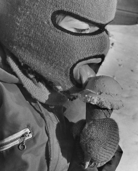 Close-up of a child in a knitted balaclava and mittens licking an ice cream cone.
