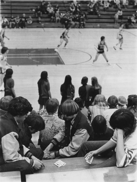 Boys playing cards in the stands at a basketball game.