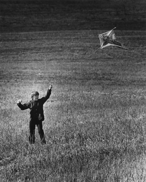 A boy flying a diamond-shaped kite in a grassy field.