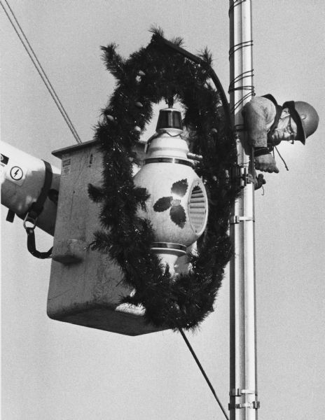 A city worker putting up holiday decorations on a light pole using a telescopic forklift.
