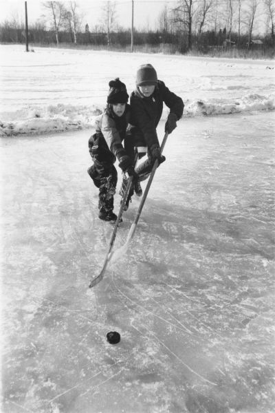 Two boys playing hockey on a skating rink.