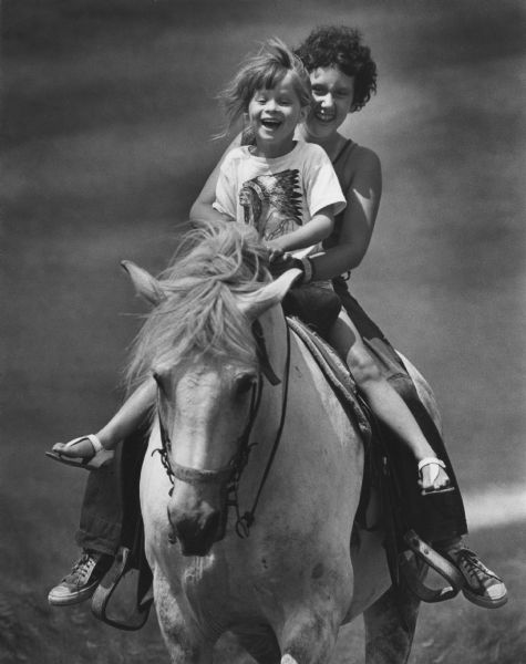 A teenager and a younger child riding a horse together.