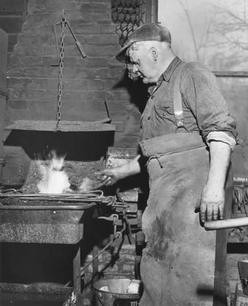 A blacksmith working at his forge. He is wearing a leather apron to protect his clothes from the heat.