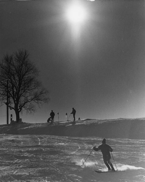 Skiers at a ski hill with the sun overhead. The flags in the snow at the top of the hill indicate that this may be a competition.