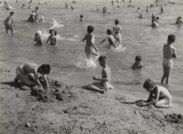 Children are playing in the water and in the sand at a beach. 
