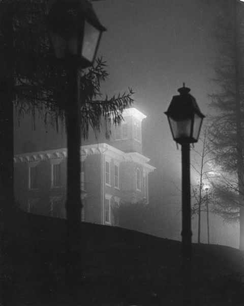Night view of the Milton College Main Hall in fog, framed by two lampposts.