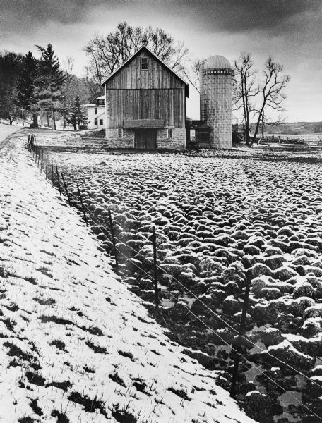 A barn and silo, on a snow covered farm along Highway 78, between Mt. Horeb and Black Earth. The farmhouse is behind the barn. A barbed wire fence lines the road.