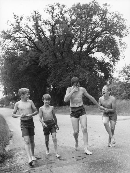 Four boys in swimsuits are laughing and smiling as they walk down a road.