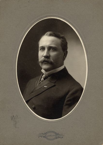 Oval-framed quarter-length portrait of Governor James O. Davidson, Wisconsin's 21st governor. He is wearing a suit and tie with an upright collar, and a sword pin on his lapel.
