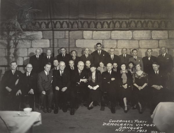 Group portrait at the Democratic Victory Banquet, celebrating the newly elected Albert G. Schmedeman (four from the right in the first row). Schmedeman sits with his arms crossed and is sitting next to his wife, Katherine Schmedeman (five in from the right), who is wearing a fur stole. Next to her sits Leo T. Crowley.