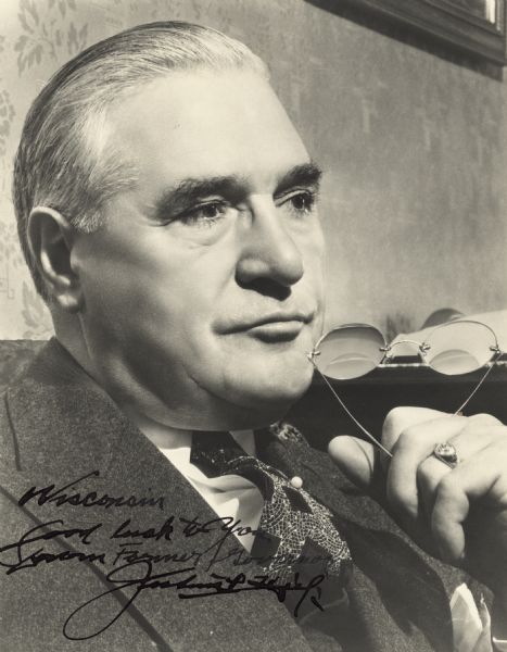 Quarter-length portrait of Julius Heil, Wisconsin's 30th governor. He is wearing a suit, and tie with a tie pin, and faces towards the right, holding his glasses in his left hand next to his chin. He wears a ring on his left hand.