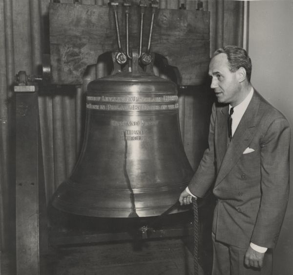 Governor Walter J. Kohler Jr. stands next to a replica of the Liberty Bell, holding a rope attached to the clapper of the bell.