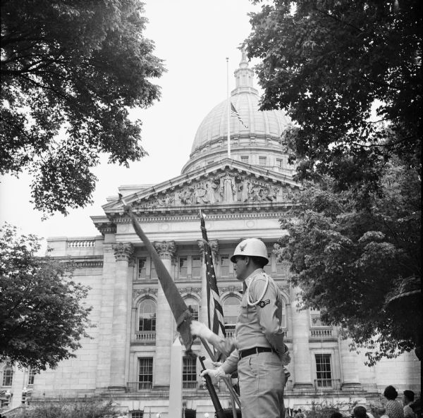 An Air Force color guard from Truax Field is in his position at the south entrance to the Wisconsin State Capitol with the Capitol flag at half mast to honor the state's war dead. To the left and behind the color guard is the cenotaph used in the wreath ceremony conducted by Madison veterans organizations and auxiliaries. Madison observed Memorial Day with a parade and three memorial services.