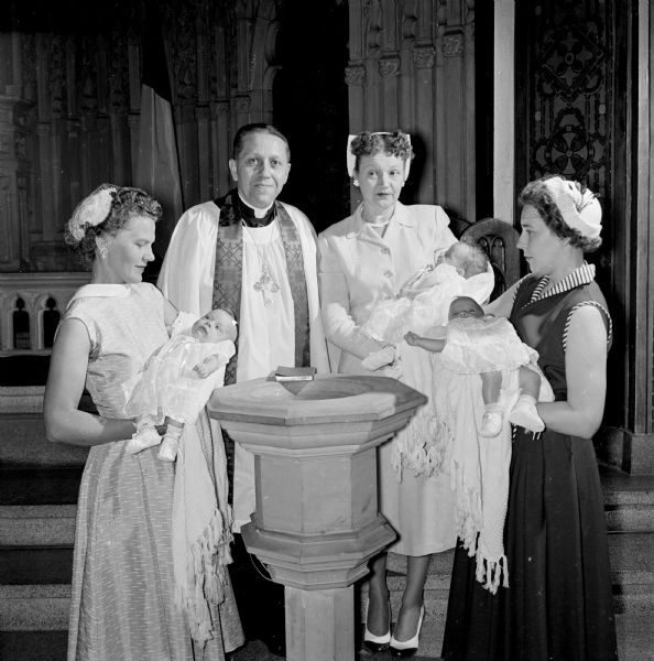 The triplet daughters of William and Joyce Wills are baptized at Luther Memorial Church. Sponsor Mrs. Morris Wills holds infant Jacqueline Diane at left, Dr. Charles Puls, pastor of the church, stands beside her, sponsor Elizabeth Stone holds infant Susan Elizabeth, and sponsor Helen Koltes holding infant Catherine Ann.
