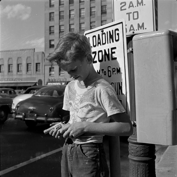 After Governor Kohler signed legislation legalizing the sale of caps and cap pistols, many youth prepared to celebrate the Independence Day holiday with the new toys. Pictured is Bill McMahon obeying the sign and loading his cap pistol in a loading zone.
