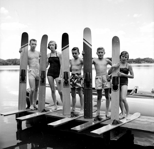 The five Feiler youngsters are posing on a dock with the tailor-made water skis that the family makes during the winter months. Left to right are John, 16; Helen, 15; Bob, 12; Steve, 13; and Sue, 13. They live and ski on Monona Bay.