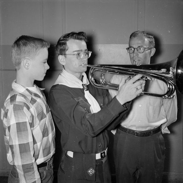 John Price (center), 2905 Monroe Street, is a member of the nationally famous senior Four Lakes Drum and Bugle Corps and bugles at a junior corps rehearsal. Joe Swanson, 309 Kensington Drive, and Roger Muzzy, an instructor, look on.