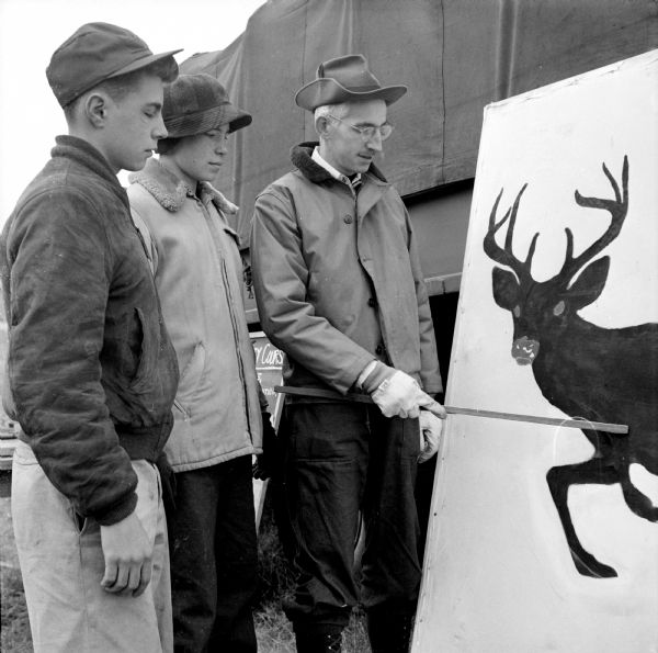 Two youthful hunters, Denny Reul and Tom Goedell of Madison, watching Jerry Teesdale pointing out the vital points a hunter must hit to get his buck at a training course in gun safety held at the Winnequah Gun Club near Lodi.