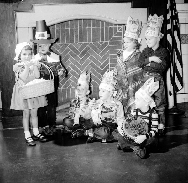 A special observance of Thanksgiving held at Randall Kindergarten featured costumed children.  At left are Linda Kay and Robert Willard as pilgrims. On the right, seated on the floor and dressed as Indian braves, are: Dick Nelson, Brian Smith and John Ohnstad. Standing behind them, also dressed as Indians, are Marilyn Wood and James Pickett.