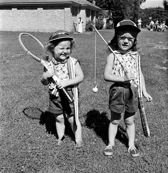 Pamela Henken and Bambi Henken pose in their matching clothing, one carrying a tennis racket and one carrying a fishing pole, during the Maple Bluff Fourth of July celebration.