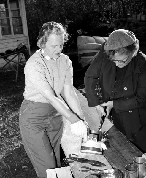 Helen Giessel, left, holds a large juice can as Avis McLean cuts it with a tin sheers to make a plate during part of an emergency mass feeding demonstration and course of instruction at Franklin Field.  During this two day event, seventy five Madison and Dane County residents will learn what to do if a community's food and water are poisoned by nuclear radiation.