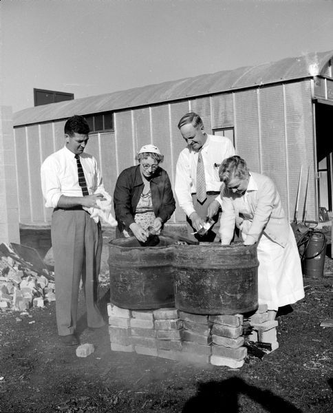 Four people demonstrate how old oil drums cut in half can be used to wash dishes as part of an emergency mass feeding demonstration and course of instruction at Franklin Field. Participants include, from left to right: Robert Nuckles, Mrs. Earl Siggelkow of McFarland, George Solsrud, and Laura Palmer. During this two day event, seventy five Madison and Dane County residents will learn what to do if a community's food and water are poisoned by nuclear radiation.