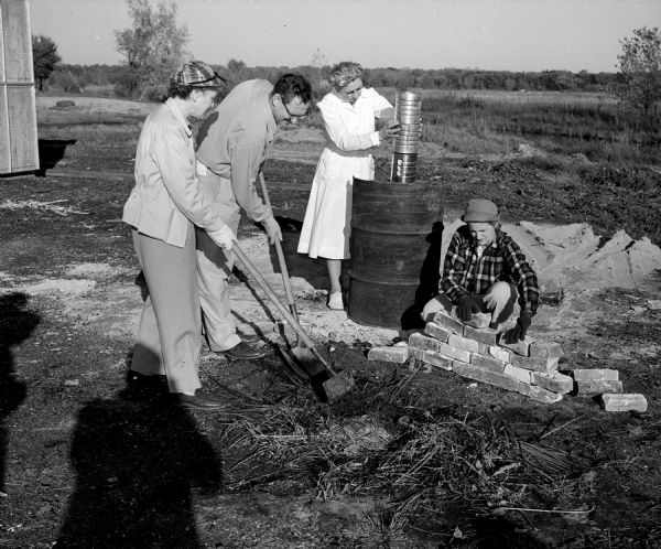 Mildred Ryerson, left, and Melvin Dykman mixing mortar for brick stoves and ovens as part of an emergency mass feeding demonstration and course of instruction at Franklin Field. Kathryn Henning is stacking large cans which will serve as a chimney for the oil drum oven, while Irma Smith is stacking bricks. At this two day event, seventy five Madison and Dane County residents will learn what to do if a community's food and water are poisoned by nuclear radiation.