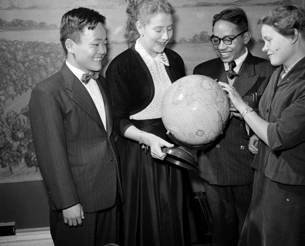 Four foreign exchange students attending Madison high schools are guests of honor at the annual Madison Youth Council banquet. They are shown pointing out their native lands on a globe. Left to right are: Hiro Yamamoto of Japan, Josephine M. Chance of England, Oscar Blantan of Indonesia, and Ritva Jantunen of Finland.