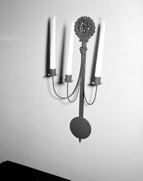 This metal wall-hanging candle holder was made from a trivet and a pendulum by Mrs. Winfield Martin for the Art Guild gift exhibit. Winfield made the candle holder with the help of her husband, a metal shop teacher.