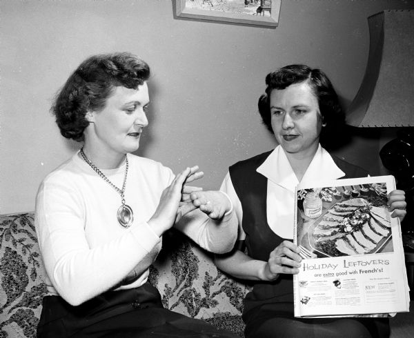 Women in a neighborhood near Dean Avenue study sign language so that more deaf women can join their homemakers' club. Mrs. Gordon Mather, left, gives the sign for meat. At the right is Carola Rasmus, instructor and the only deaf women shown. Her husband, Ray, is a Madison Newspaper composing room employee.