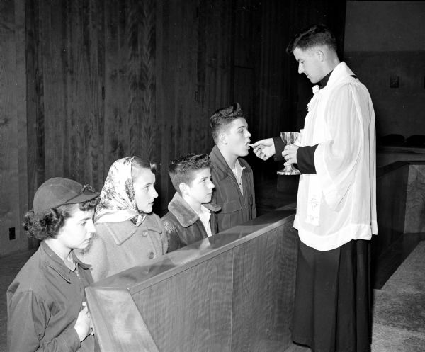 Reverand Vincent Browne, spiritual adviser to the Chi Rho group at Our  Lady Queen of Peace Catholic Church, serves Communion to four youth participating in National Communion Sunday. The youth are Ellen Vandervest, Judy Rowley, Robert Kuehn, and Jerry Falci.