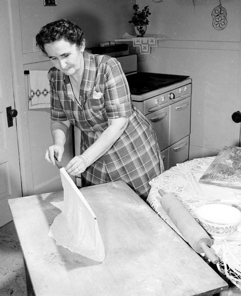 Three sisters gather at one of their homes to carry on a 30 year Christmas time tradition of making a year's supply of lefsa. Mrs. Roy J. Nelson, 145 Marquette Street, uses a stick known as a "floyve" to carry the sheets of lefsa from the table to the stove. The stick is also used to turn the lefsa while it bakes. She and her two sisters gathered at one of their homes to carry on a 30 year Christmas time tradition of making a year's supply of lefsa.