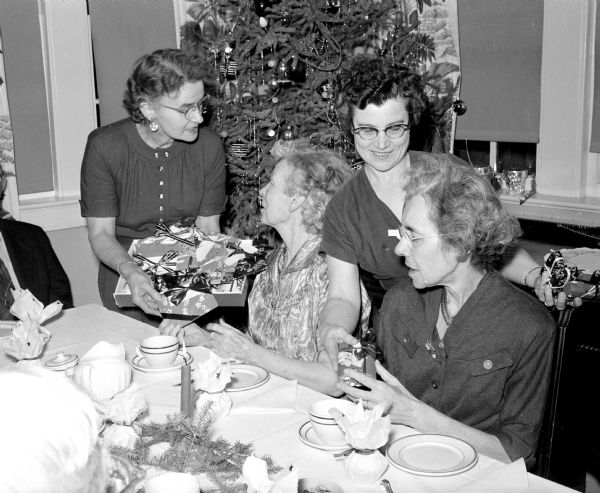 Elizabeth Damres (left), home matron, and Helen Antoine, Mendota Garden Club member, pass out gifts during a Christmas party for residents of the Oakwood Lutheran Home. Residents are Pearl Roe, left, and Mrs. Conrad Retelsdorf.