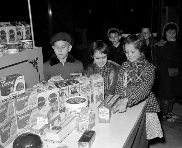 School children from the Madison area are among the first visitors at the opening of the $100,000 Dairy Caravan at the State Capitol. One display shows the various ways of packaging dairy products. Shown observing the display are, (left to right): Johnny Lovick, Kathy Edwardson, and Suzy Culbertson from the DeForest School.