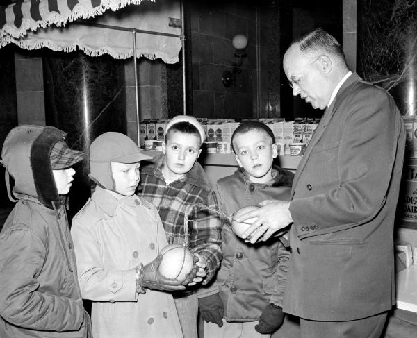 School children from the Madison area are among the first visitors at the opening of the $100,000 Dairy Caravan at the State Capitol. Maple Grove pupils observe cheese balls explained by Dane County Judge George Kroncke, Jr. (right). The students are, (left to right): John Stokestad, Gerry Durgin, and Gerry Lintvedt.