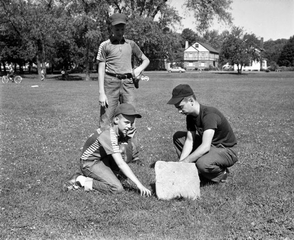Bob Merry (kneeling, left) helps Umpire Pat McCormick adjust the base as Kenny Kissenger looks on in preparation for a baseball game.