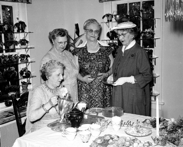 Jessie Briese, sitting, is pouring tea for (left to right) Lillian Dean, Mrs. John Westmont, and Agnes Dreher. The tea and jelly mart was held at the home of Forrest and Loretta Iler and sponsored by the White Shrine of Jerusalem to earn money for various philanthropic projects.