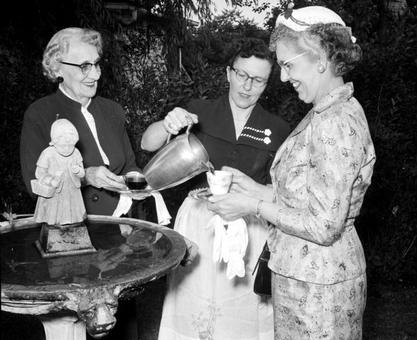Refreshments are served outdoors at the summer tea and jelly mart sponsored by Madison Shrine, No. 6, of the White Shrine of Jerusalem.  Ruth Blood (center) is pouring tea for guests Anna Berg (left) and Gladys Castle in the yard of the Iler home.