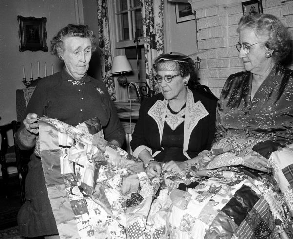 Attending a tea honoring long time members of Christ Child Club Circles are, left to right, Margaret Purcell, Laurine Bridge and Alice Gregg. They are looking over one of the more than 900 bed quilts which a circle has tied over the years. The club is a Catholic organization comprised of eight active circles committed to the service of children.
