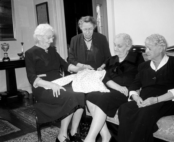 Attending a tea honoring long time members of Christ Child Club Circles are, left to right, Jeanette Foran, Mary Gox, Margaret Straub, and Rachel McKee. They are looking at a child's garment, sewn by members of a circle. The club is a Catholic organization comprised of eight active circles committed to the service of children.