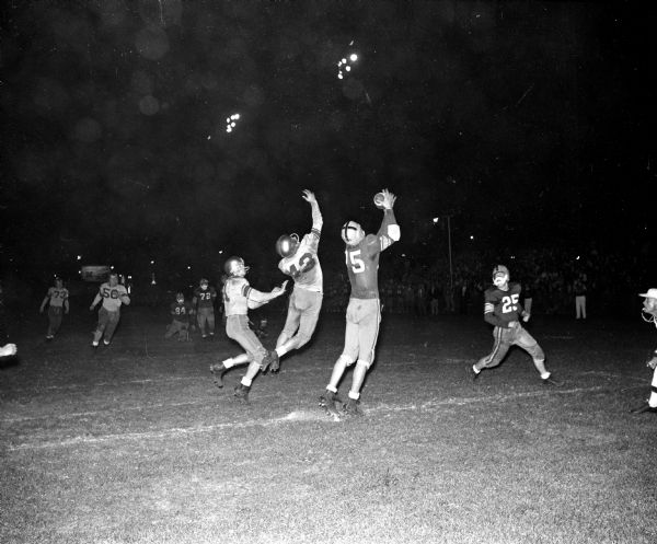 Madison East High School's Gordy Hart (75) catches a pass from quarterback Ron Staley for a touchdown against Madison West High School. Other East players include Tom Rich (25), Dave McCloskey (84), and Jon Rockstad (72). The Madison West defender is Ray Denson (43).