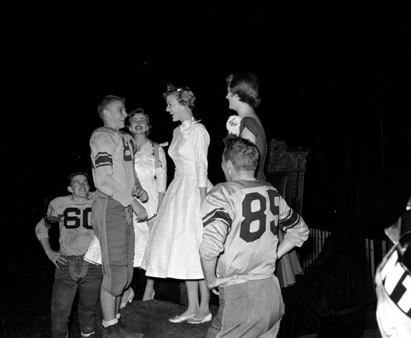 Madison West High School player Don Quam (81) crowns the homecoming queen, Joan Herreid, at the Madison West High School versus Madison East football game. The queen's attendants include Diane Fellows, left, and Kay Johnson. The other players in the picture are Ken Johnson (60) and John McKenna (85).
