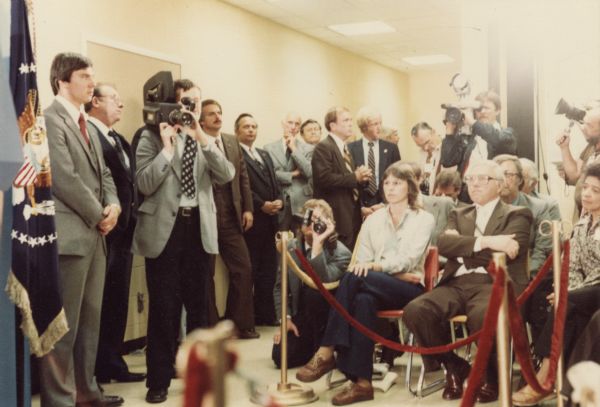 Group of people standing and sitting behind a velvet rope listening to President Jimmy Carter speak. Vel Phillips sits on the far right.