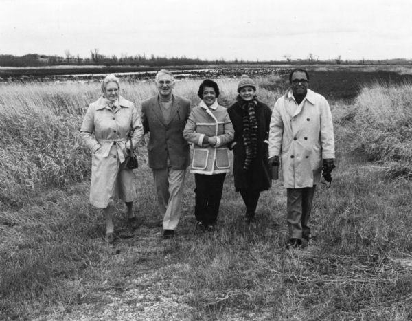Group portrait at Horicon Marsh. Vel Phillips stands in the middle of the group wearing a coat and dark pants. The man on the far right is W. Dale Phillips, also wearing a coat and holding binoculars. From the left is Dorothy Mueller, George Kosich, and between Vel and W. Dale Phillips is Mrs. Kosich.