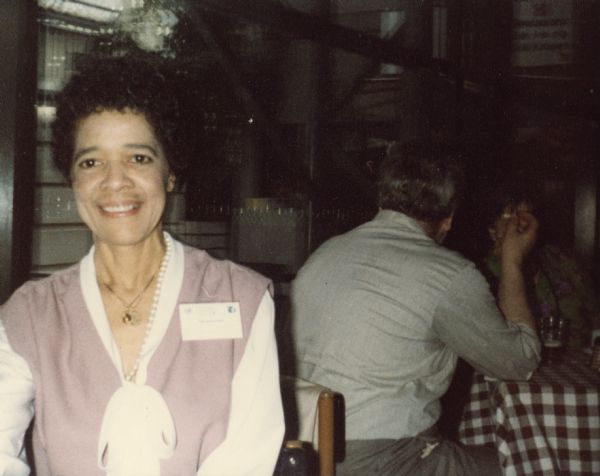 Vel Phillips wearing pearls and a name tag sitting at a table.
