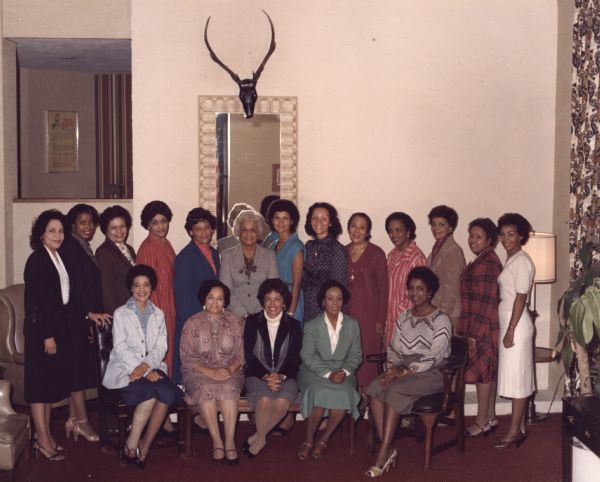 Vel Phillips sitting on the far left in first row of a group portrait. Her right leg is wrapped. A line of women stand in the second row.