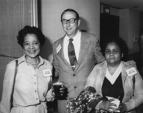 Vel Phillips stands on the left holding a drink and wearing a name tag reading: "Secretary of State." In the center is George Goetz, and on the right is Representative Marcia P. Coggs.