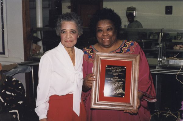 Vel Phillips standing beside Jeannetta Robinson. Jeannetta is holding a plaque that awards the James Howard Baker Award to Career Youth Development, Inc. from the Community Brainstorming Conference.