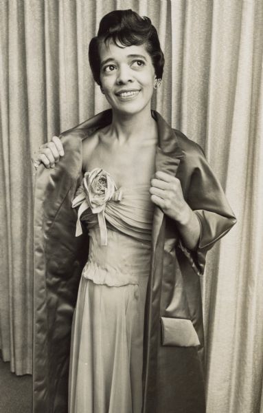 Three-quarter length portrait of Vel Phillips wearing a strapless dress with a flower detail in the middle. She is also wearing a satin coat and earrings.